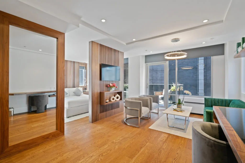 Bright Gotham Hotel NYC suite living area with hardwood floors, lounge chairs, green sofa, and balcony doors