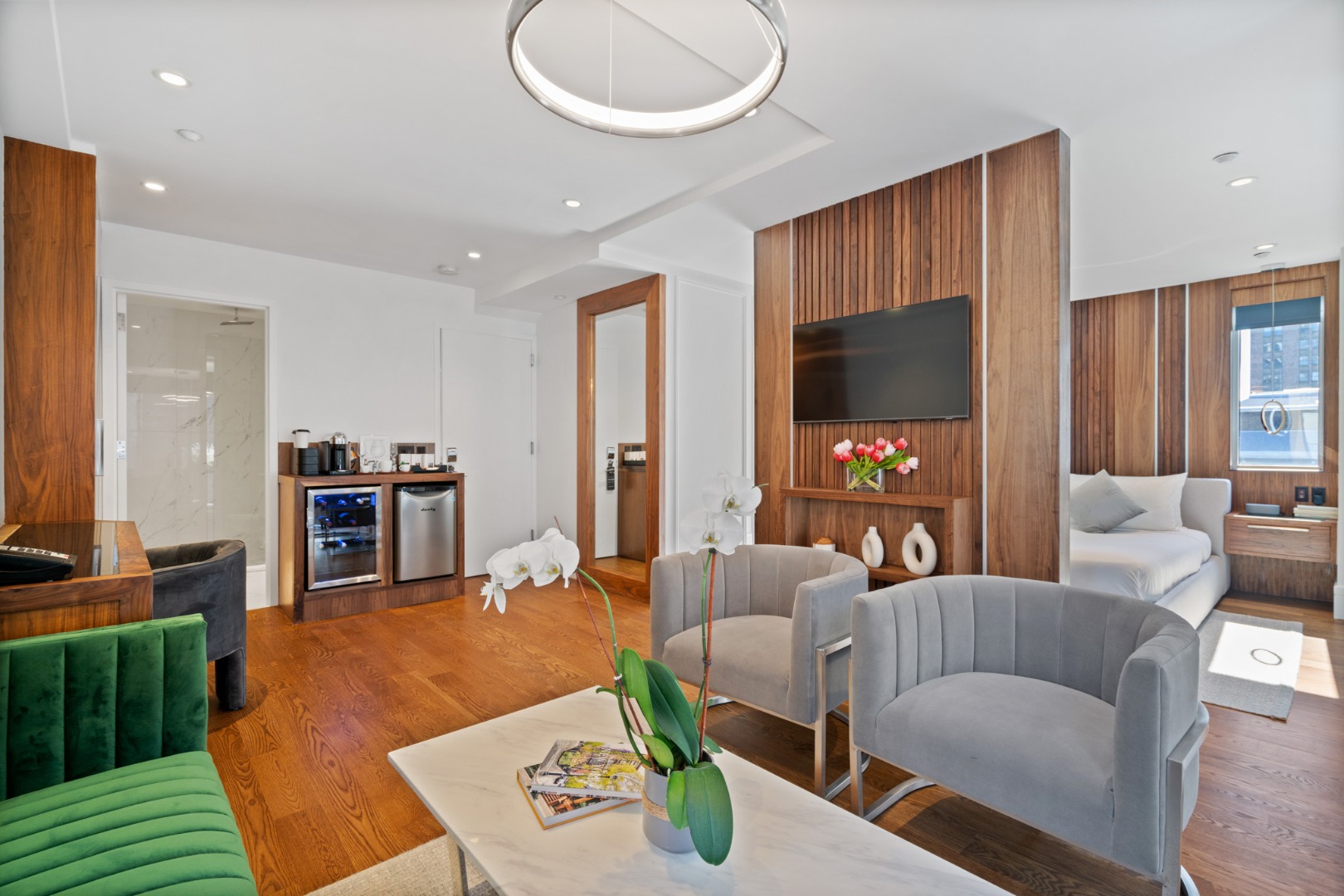 A wide view of a modern hotel room with living area, kitchenette, and bed.